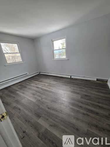 A room with wooden flooring and two windows.