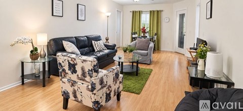 A living room with a black couch, a grey armchair, a floral chair, and a glass table with a vase of flowers on it.