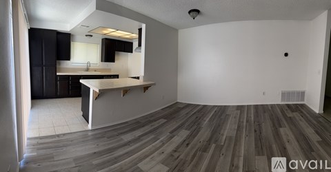 A room with wooden flooring and a kitchen area in the background.