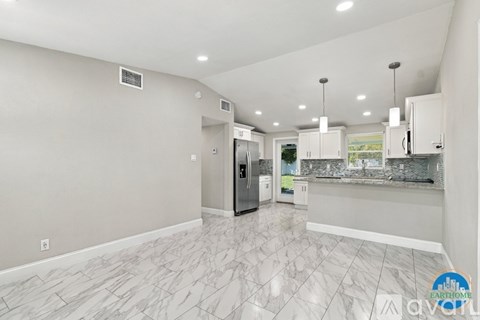A spacious kitchen with a marble floor and a refrigerator in the middle.