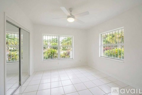 A room with a ceiling fan and two windows overlooking a green area.