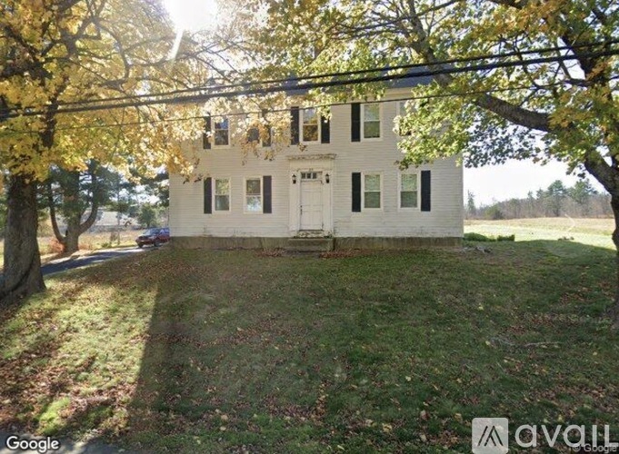A white house with a black roof and a tree with yellow leaves in front of it.
