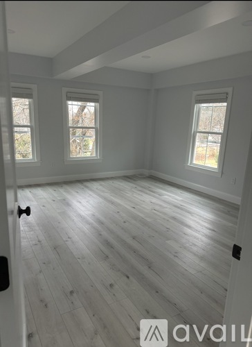A room with wooden flooring and three windows.
