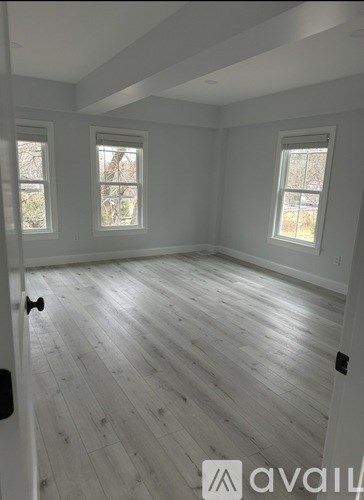 A room with wooden flooring and three windows.
