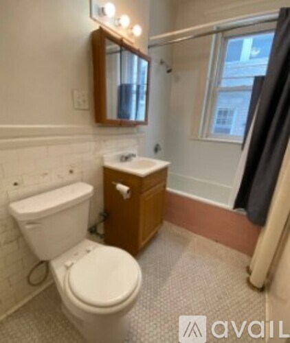 A bathroom with a toilet, sink, mirror, and a window.