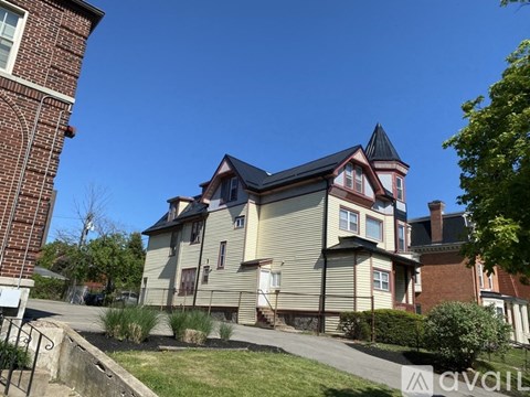 A house with a red brick building to the left and a house with a brown roof and a tower to the right.