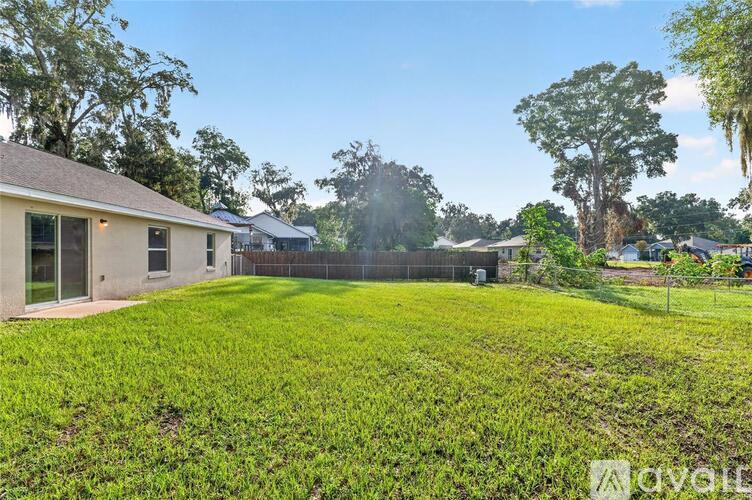A grassy yard with a house and trees in the background.