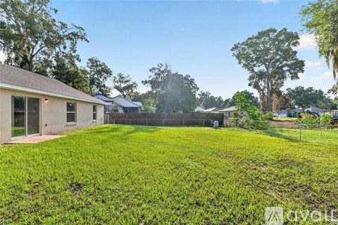 A grassy yard with a house and trees in the background.