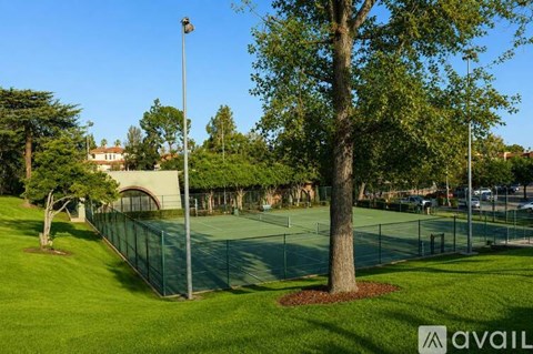 A tennis court surrounded by a green fence and trees.