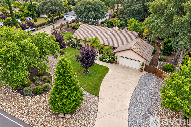 A house with a brown roof is surrounded by a gravel path and green trees.