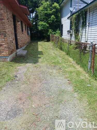 A gravel pathway leads from a brick building to a white house.