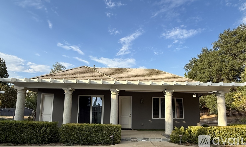 A house with a grey roof and white columns stands under a blue sky.
