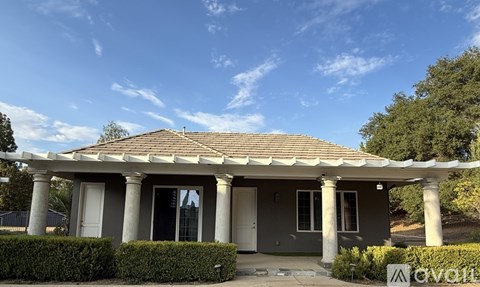 A house with a grey roof and white columns stands under a blue sky.