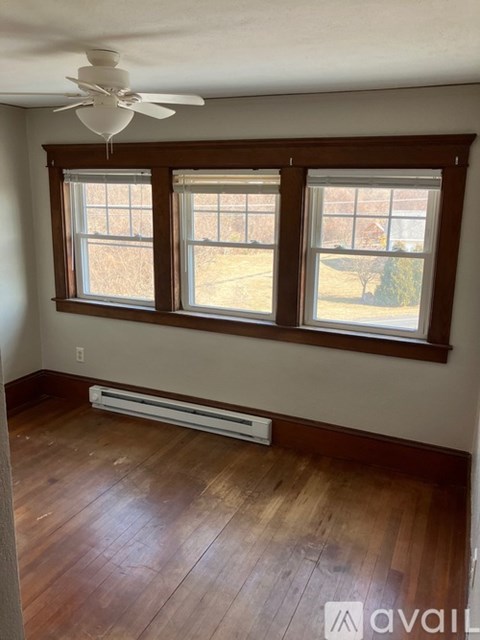 A room with a ceiling fan and a window with a view of a fence and trees.