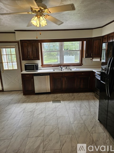 A kitchen with a black refrigerator and a ceiling fan.