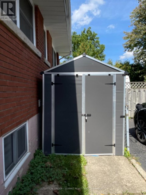 A small grey shed sits in front of a red brick house.