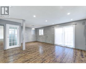 A spacious room with wooden floors and white walls, with a door on the left and a window on the right.