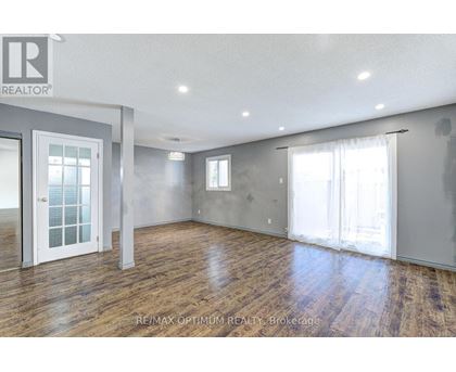 A spacious room with wooden floors and white walls, with a door on the left and a window on the right.