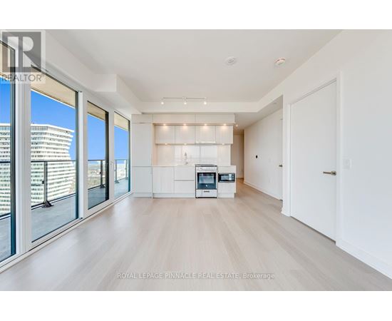 A spacious, well-lit living room with a kitchenette in the background.