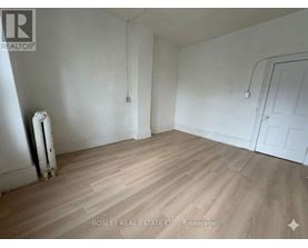 A room with wooden flooring and white walls, with a door on the right side.