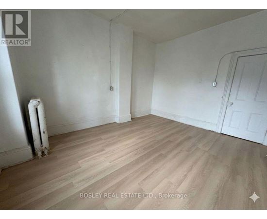 A room with wooden flooring and white walls, with a door on the right side.