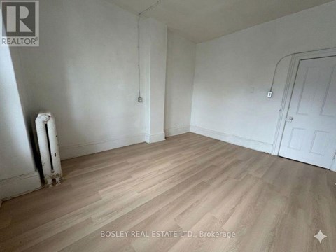 A room with wooden flooring and white walls, with a door on the right side.