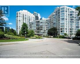 A large, modern apartment complex with a well-maintained lawn and trees in the foreground.