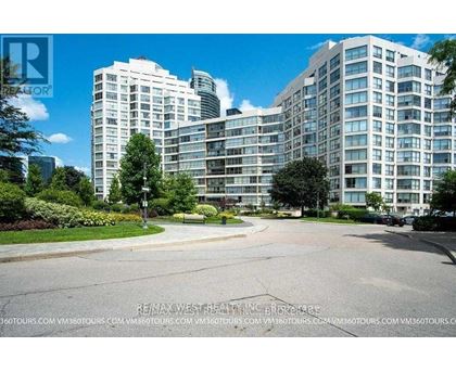 A large, modern apartment complex with a well-maintained lawn and trees in the foreground.