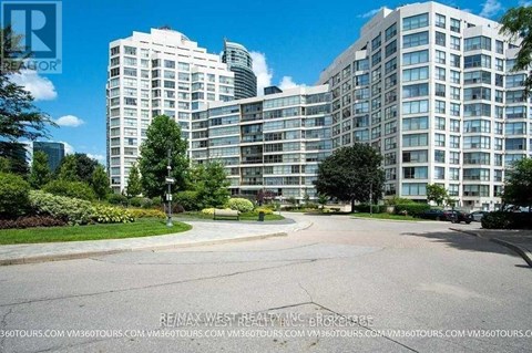 A large, modern apartment complex with a well-maintained lawn and trees in the foreground.