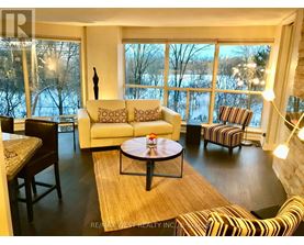 A living room with a large window and a view of trees and water outside.