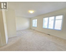 A spacious room with a carpeted floor, two windows, and a ceiling light fixture.
