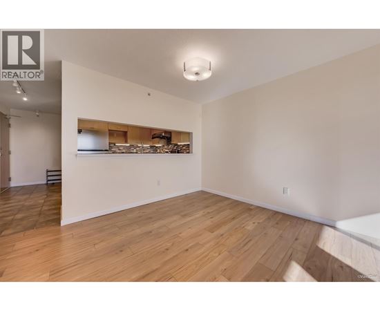 A large empty room with wooden flooring and a white wall.