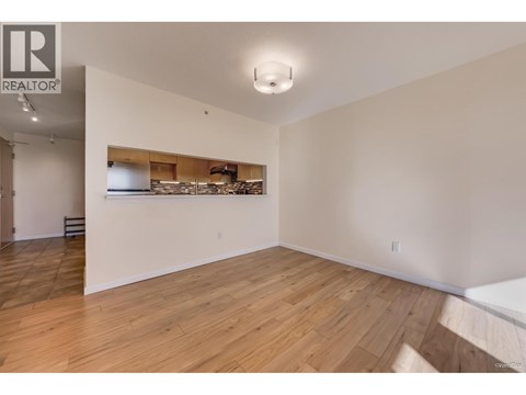 A large empty room with wooden flooring and a white wall.