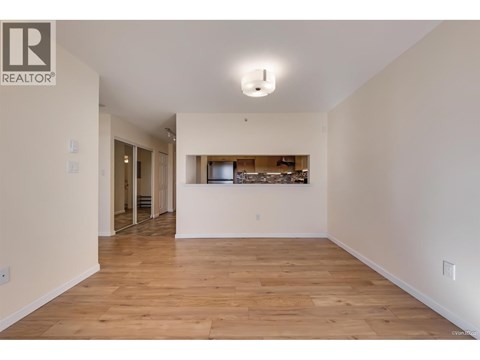 A spacious room with wooden flooring and a bar area in the background.