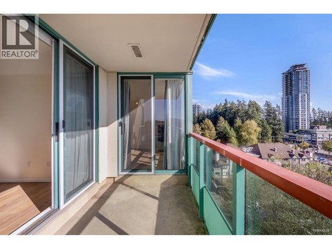 A balcony with glass railings and sliding doors overlooks a cityscape.
