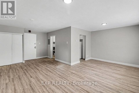 A room with wooden flooring and white walls, with a door on the left and a closet on the right.