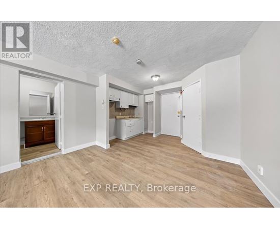 A room with wooden flooring and white walls, with a door on the right side.
