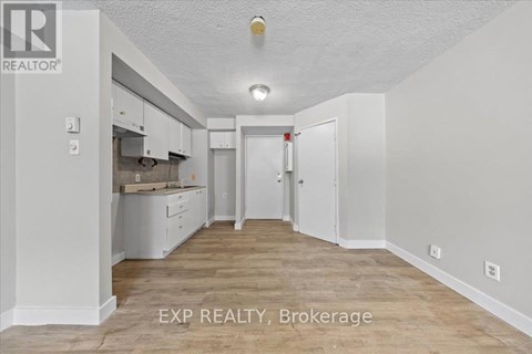 A white room with a kitchen area and a brokerage sign.