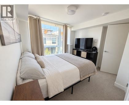 A bedroom with a large bed, a television, and a window with curtains.