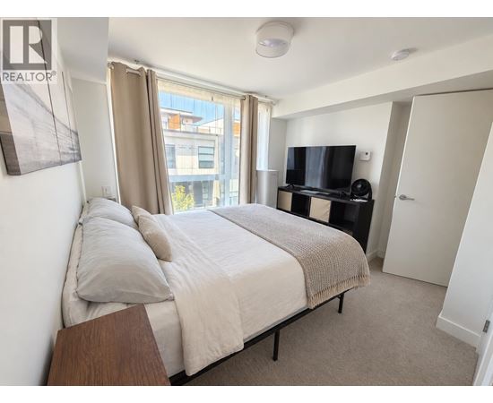 A bedroom with a large bed, a television, and a window with curtains.