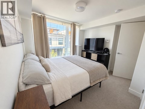 A bedroom with a large bed, a television, and a window with curtains.