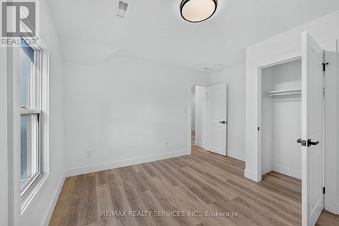 A room with wooden flooring and white walls, with a door on the right and a window on the left.