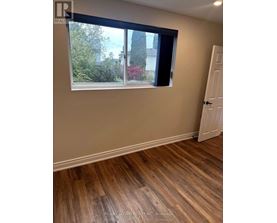 A room with a wooden floor and a window showing a view of trees and a house.