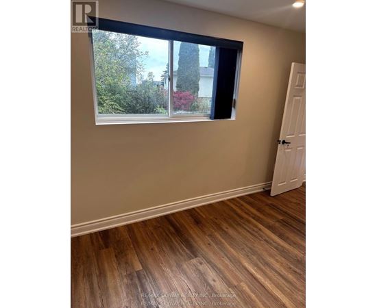 A room with a wooden floor and a window showing a view of trees and a house.