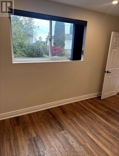 A room with a wooden floor and a window showing a view of trees and a house.