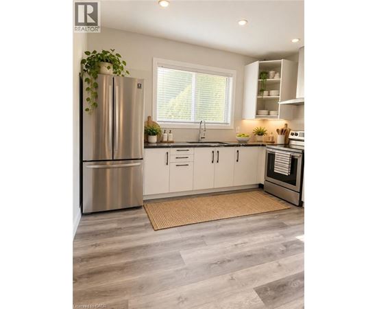 A modern kitchen with a stainless steel refrigerator and wooden flooring.