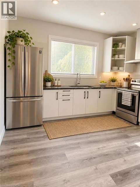 A modern kitchen with a stainless steel refrigerator and wooden flooring.