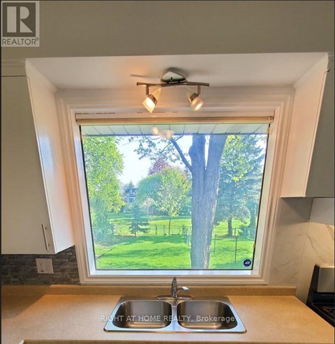 A kitchen with a sink and a window overlooking a green lawn.