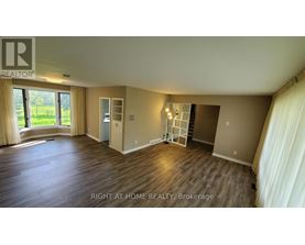 A spacious room with wooden flooring and a large window with curtains.