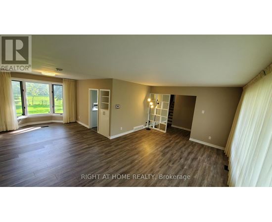 A spacious room with wooden flooring and a large window with curtains.